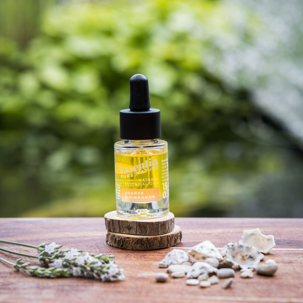 Doorzichtig flesje met estheirische olie orange en cinnamon geur. Staand op twee houten schijfjes met een frisse blur achtergrond.