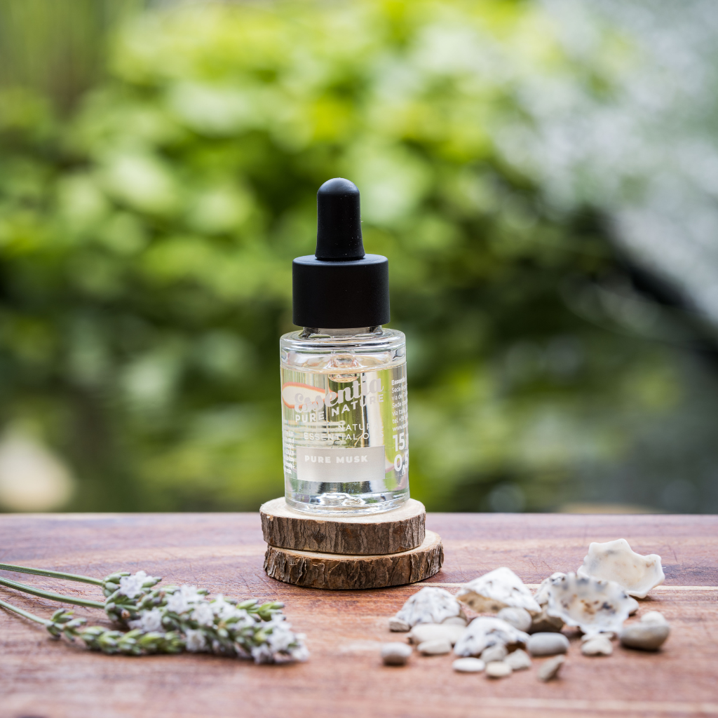 Doorzichtig flesje met estheirische olie pure musk geur. Staand op twee houten schijfjes met een frisse blur achtergrond.