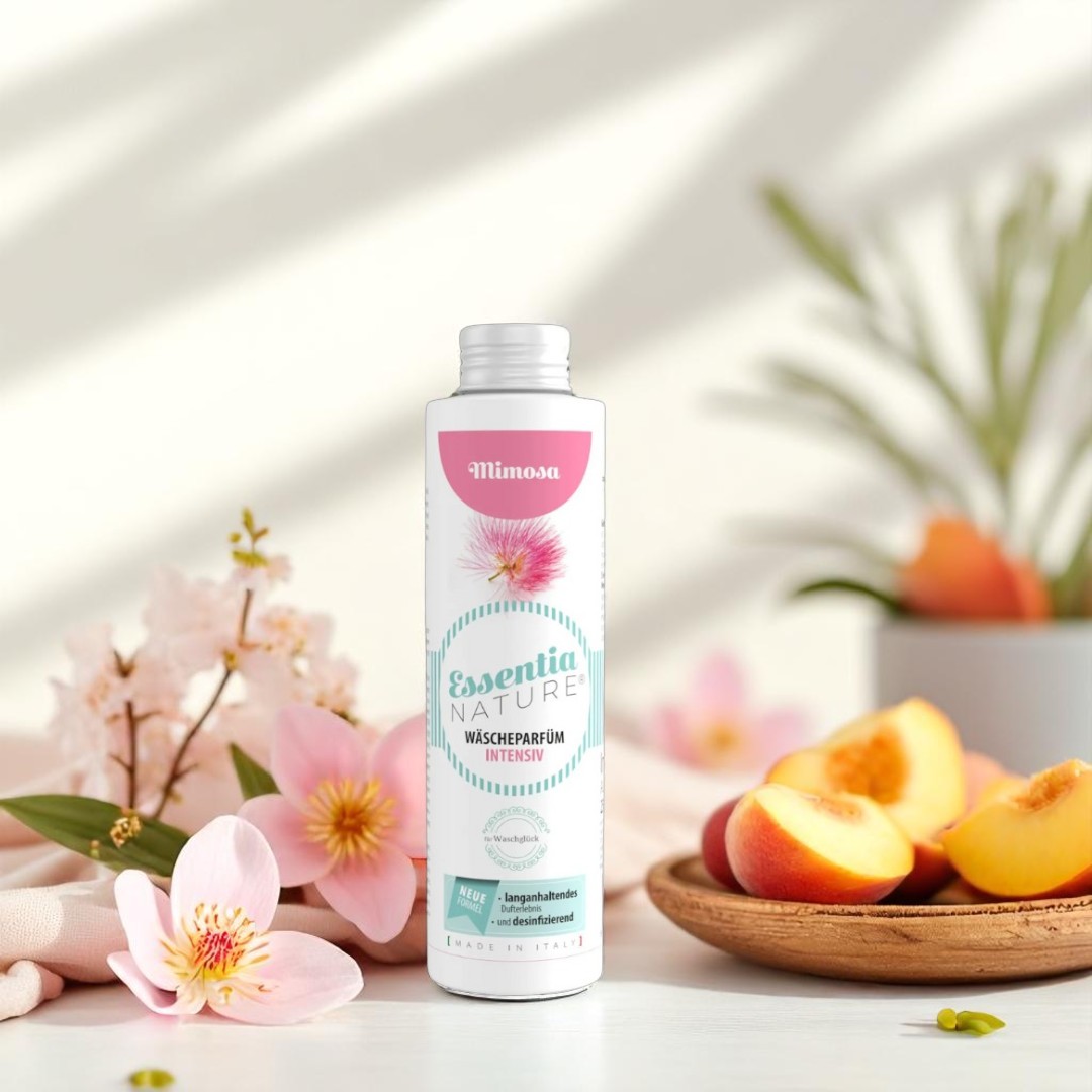 Essentia Nature Mimosa wasparfum fles tussen zachte roze bloemen en verse perzikpartjes in een lichte, luxe setting voor een langdurige, frisse wasgeur.