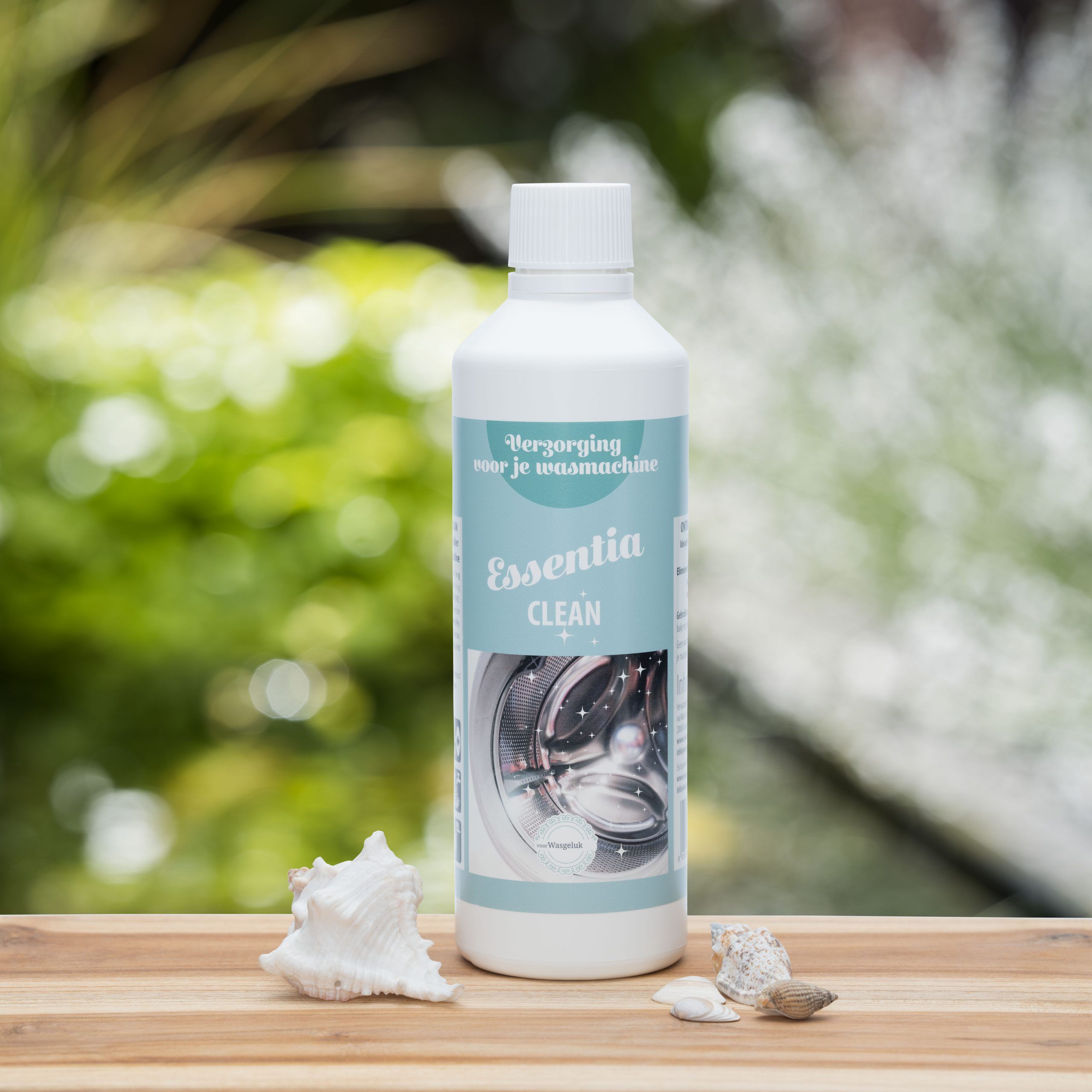 Witgroene fles Wasgeluk Essentia Clean wasmachine reiniger en verzorging, duurzaam en microplasticvrij, staand op houten tafel met schelpen tegen een groene natuurlijke achtergrond.