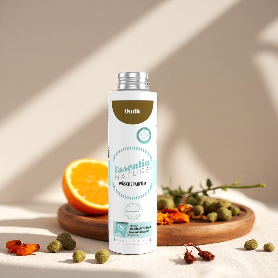 Essentia Nature Oudh wasparfum van Wasgeluk in witte fles met turquoise details, omringd door sinaasappel en natuurlijke ingrediënten voor een duurzame, microplasticvrije en langdurige luxe wasgeur.