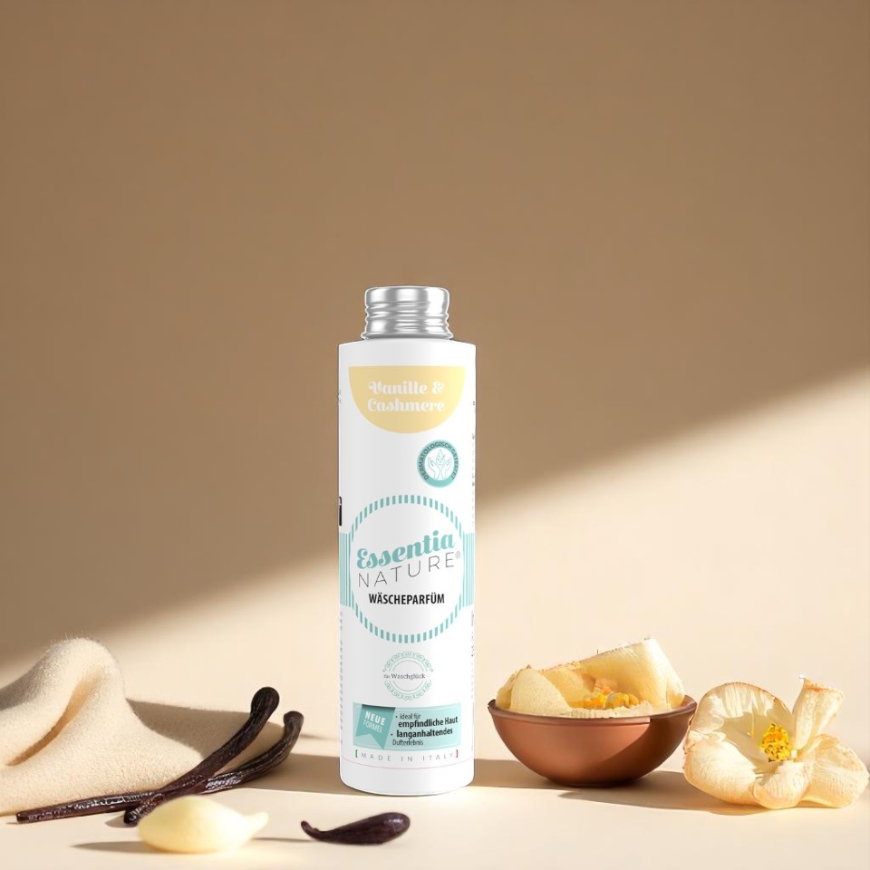 Essentia Nature wasparfum Vanille & Cashmere in witte fles met turquoise en gele accenten, omringd door vanillestokjes en zachte bloemen op een beige achtergrond voor een luxe, microplasticvrije geurbeleving.