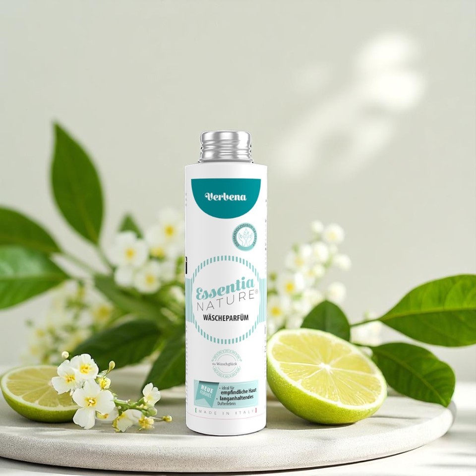 Essentia Nature wasparfum Verbena van Wasgeluk in een witte en turquoise fles, gefotografeerd tussen limoenschijfjes en witte bloesem voor een frisse, natuurlijke en microplasticvrije wasgeur.