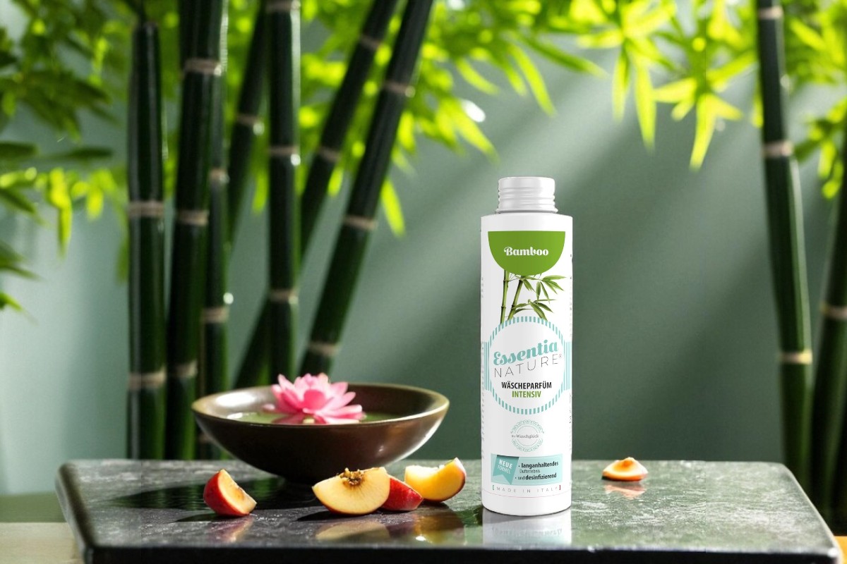 Essentia Nature Bamboo wasparfum intensief op een zwarte steenplaat met bamboe, lotus en perzikpartjes op de achtergrond, voor een duurzame, microplasticvrije wasbeleving met langdurige luxe geur.