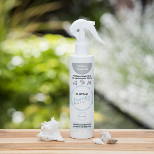 Essentia Nature Weisser Moschus hooggeconcentreerde spray met desinfecterende werking van Wasgeluk, luxe wasparfum in witte fles met vernevelaar op houten tafel met schelpen en groene, natuurlijke achtergrond.