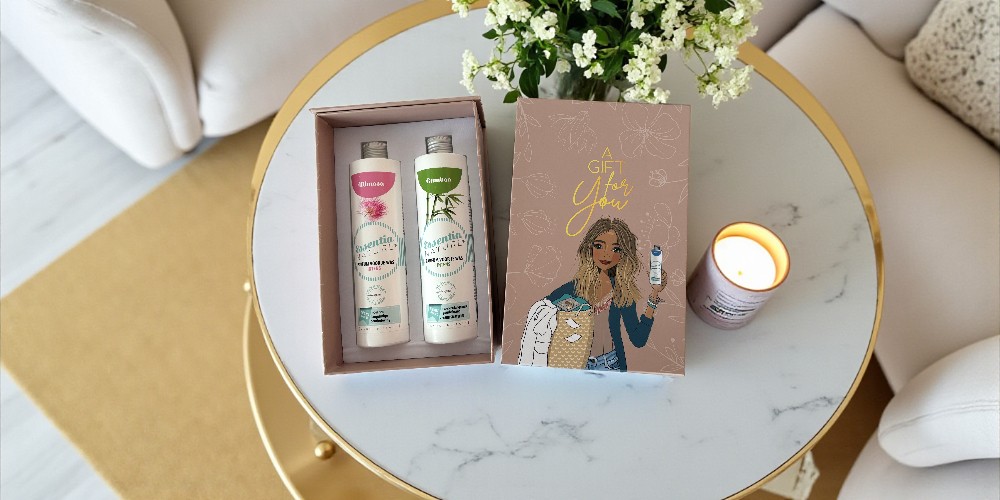 Wasgeluk cadeauset met twee flessen duurzame, microplasticvrije wasparfum in een luxe giftbox met illustratie, naast een brandende geurkaars en bloemen op een ronde salontafel.